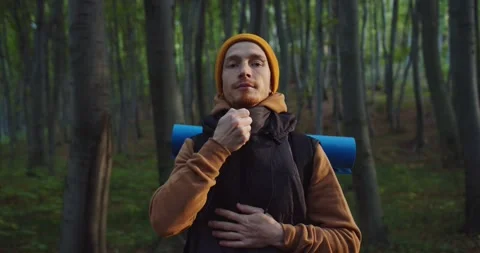 Close up of young man standing in forest snaping zipper on sports jacket and Stock Footage 154172249