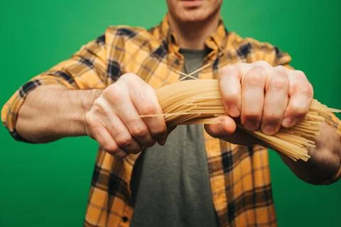 Close up young man strongly breaks spaghetti, isolated on green background Stock Photos