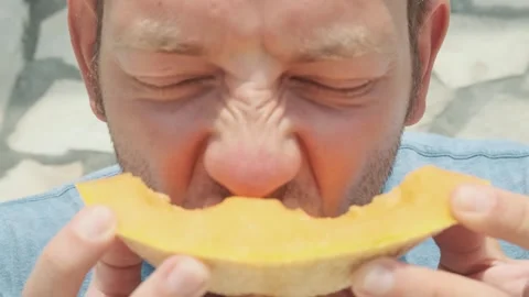 Close up of young man take a bite of fresh ripe melon cantaloupe in hot summer Stock Footage 270094847