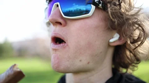 Close-up of a young man taking a big bite of a chocolate bar outdoors. The shot  Stock Footage 306000133