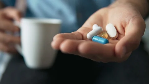 Close-up of a young man taking pills while drinking a glass of water at home Stock Footage 128963516
