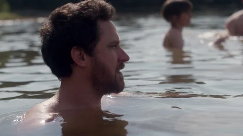 Close-up of a young man talking with his friends while floating in a forest lake 스톡 동영상 116724513