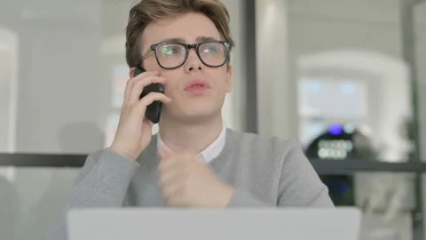 Close up of Young Man Talking on Phone while Working on Laptop Stock Footage 164878430