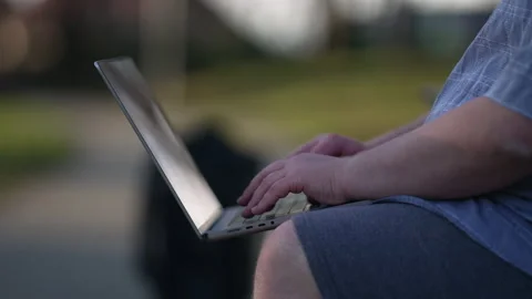 Close up young man typing on laptop sitting outside at park. One chubby cas.. Video stock 233347612