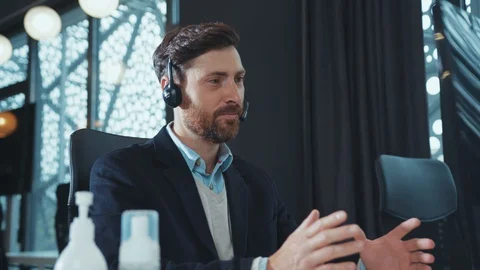 Close up young man uses headphone for work speaking on computer smiling in Video stock 130001262