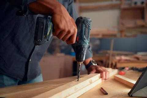 Close-up of young man using drill on wooden plank on top of table in woodworking Stock Photos