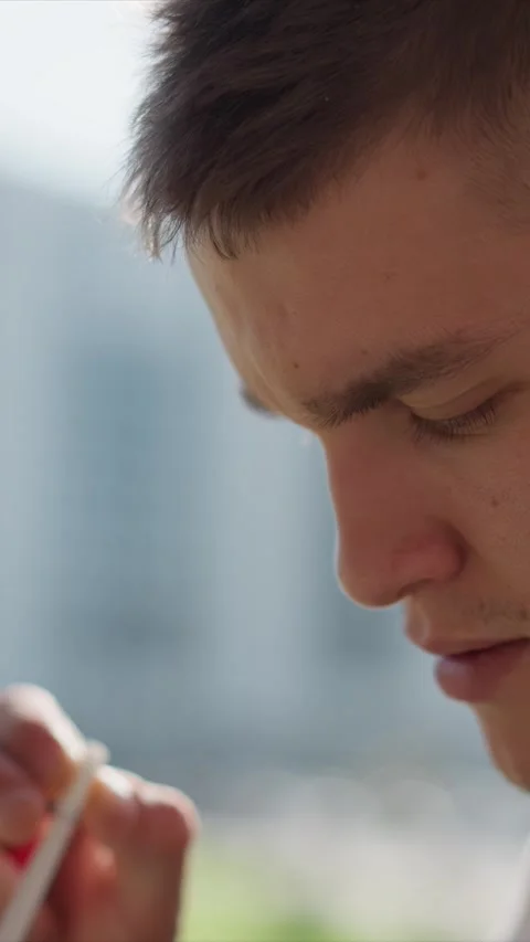 Close up of young man using electronic cigarette outdoors with soft daylight and Stock Footage 345050536
