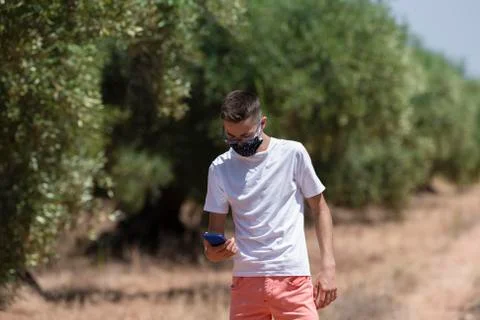 Close up of a young man using a face mask looking down at his phone on an out Stock Photos