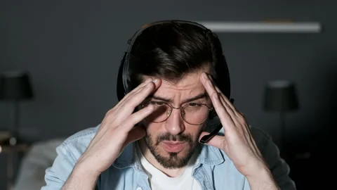 Close-Up of a Young Man Using a Laptop, Talking through a Headset Stock Footage 144374490