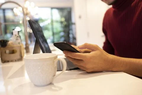 Close up young man using smart phone at laptop in kitchen 스톡 사진