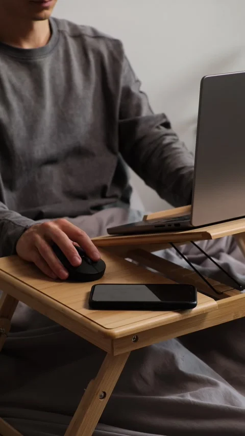 Close-up of young man working in bed on laptop with smartphone and mouse, cozy Stock Footage 314893460
