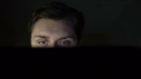 Close up of young man working on his computer in the dark. Black background Stockbeeldmateriaal 73897309