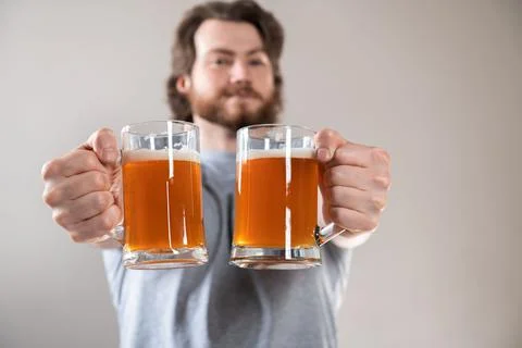 Close-up of a young man's hand with two mugs of beer isolated on light gray b Stock Photos