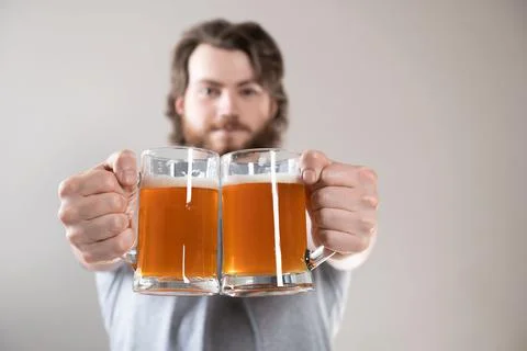 Close-up of a young man's hand with two mugs of beer isolated on light gray b Stock Photos
