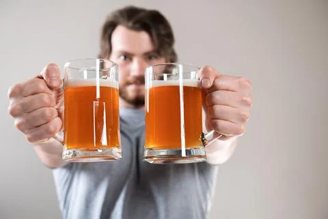 Close-up of a young man's hand with two mugs of beer isolated on light gray b Stock Photos