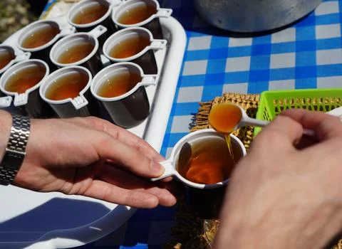 Close-up of a young man's hands adding a spoonful of floral honey to herbal.. Fotos de archivo