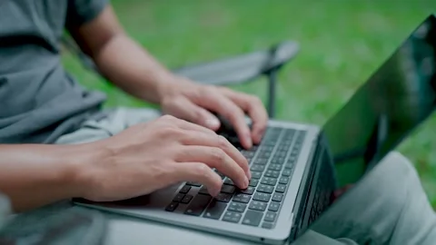 Close-up of a young man's hands sitting in a work chair on a laptop in nature. Stock Footage 283186446