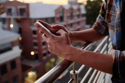 Close-up of young multiracial man in checkered shirt using phone on balcony of Stock Photos