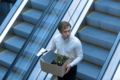 Close-up of a young office worker fired from work going down the escalator wi Stock Photos