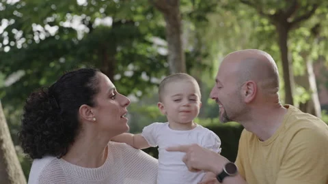 Close-up of young parents playing and kissing their little girl on a park bench Stock Footage 226676868