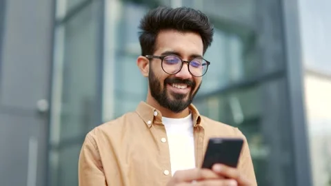 Close up. A young smiling man is using a smartphone while standing on the street Stock Footage 246995450