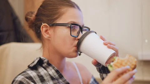 Close up of young woman drinking coffee while eating food in indoor setting with Stock Footage 346738909