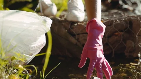 Close-up of young woman picking up litter into plastic bag from polluted pond Stock Footage