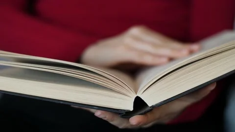 Close-up of young woman with red pullover reading hardcover book at home. Stock Footage 142842482