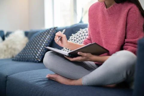 Close Up Of Young Woman Relaxing On Sofa At Home Writing In Journal Stock Photos