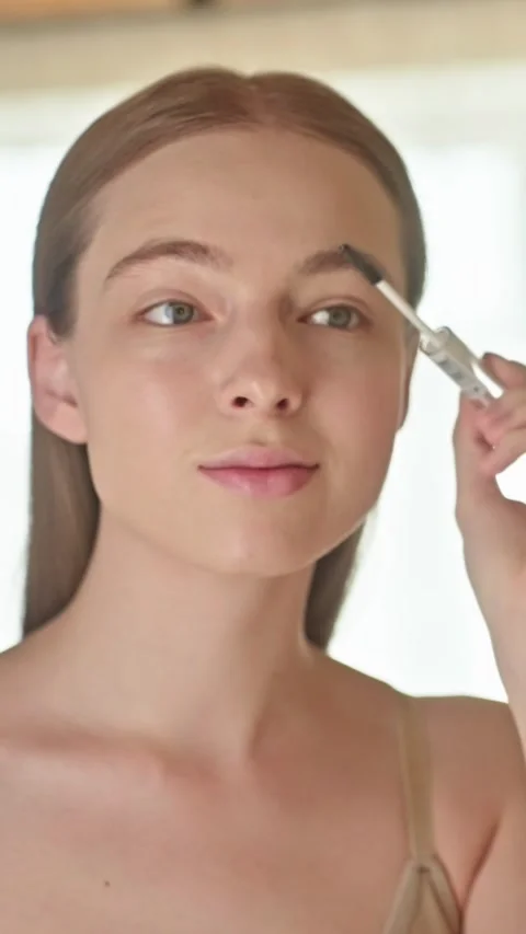 Close-up of a young woman styling her eyebrows with clear brow gel or wax. Stock Footage 312901876