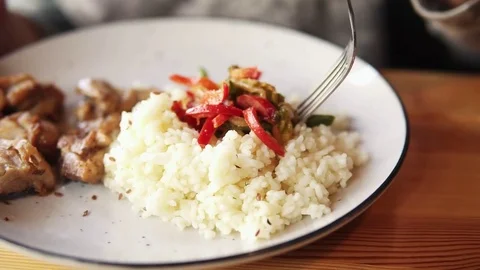 Close up of a young woman using fork to take fried meat with rice from her plate Stock Footage 82294818