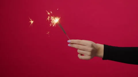Close-up of a young woman's hand holding burning sparklers on a red background Stock Footage 293166398