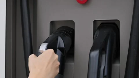 Close-up of young woman's hand puts an electric car charging port at public Stock Footage 212025223