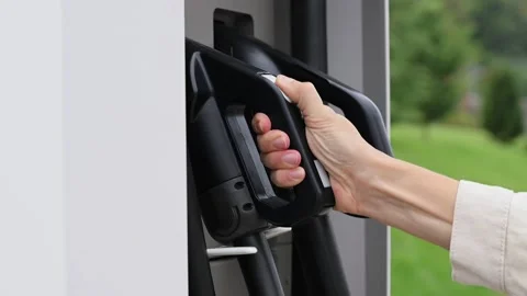 Close-up of young woman's hand taking charging port of electric car at public Stockbeeldmateriaal 212025040