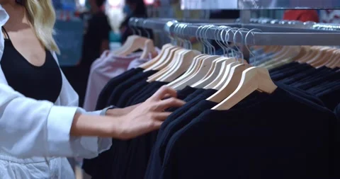 Close-up young woman's hands choosing stylish clothes hanging on hangers in Stock Footage 233315871