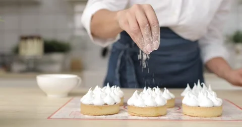 Close-up of young woman's hands pouring coconut flakes over cooked cakes. In the Stock Footage 166573564