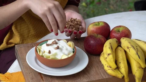 Close up of young woman's hands putting crunchy granola into yogurt bowl. 4K Stock Footage 147940778