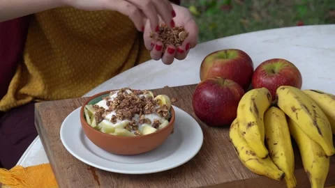 Close up of young woman's hands putting crunchy granola into yogurt bowl . 4K Stock Footage 147940792