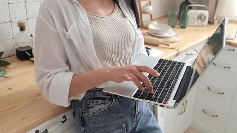 Close-up of young woman's hands typing on laptop keyboard, resting on a kitchen Stock Footage 274885116