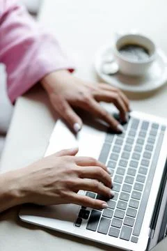 Close-up of a young woman's hands working on laptop with coffee Stock Photos