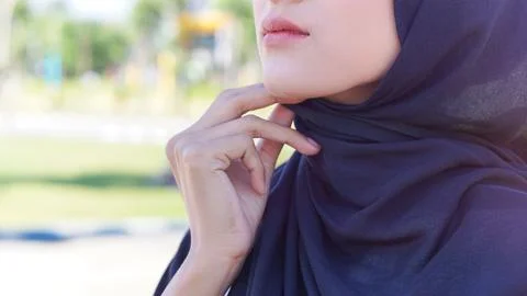 Close-up of a young woman's lower face and hand adjusting her hijab Stock Photos