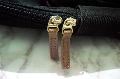 Close up on the zipper of a black bag featuring two brown leather zipper pu.. Stock Photos