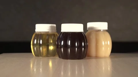 Close up zoom out of three plastic jars of different kinds honey on table Stock Footage 220482517