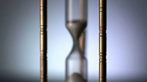 Close-up zoom-in shot of vintage metal hourglass spinning against gray Stock Footage 75959953