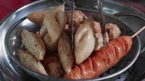 Closed up on Asian merchant hands is deep fried meatballs in a pot of boiling Stock Footage 263640784