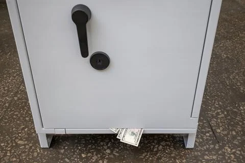 A closed ATM safe with five-dollar bills sticking out from under the door. Stock Photos
