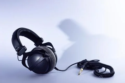 Closed-back studio headphones with a coiled  cable stand sideways on a white  Stock Photos