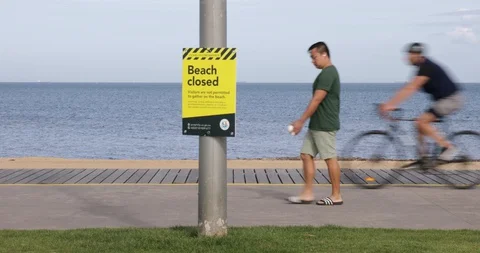 Closed Beach Sign with Man Walking and Fast Cyclists COVID 19 Coronavirus Stock Footage 128939292