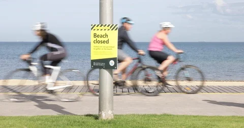 Closed Beach Sign with Many Cyclists and Walkers COVID 19 Coronavirus Stock Footage 128940045
