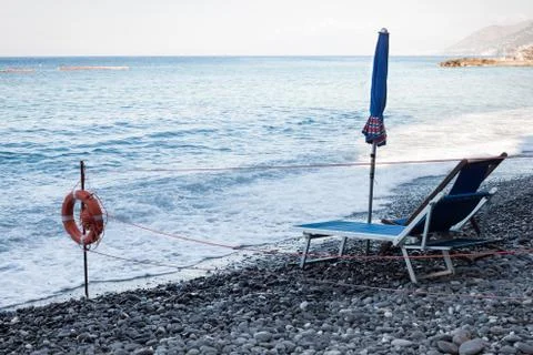 Closed beach umbrella and empty deckchair Stock Photos
